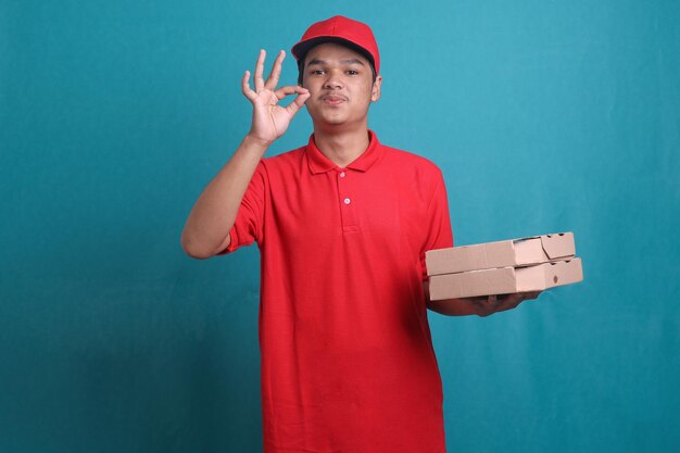 Bezorger in rood uniform houdt een doos pizza vast en doet het kusgebaar van de chef