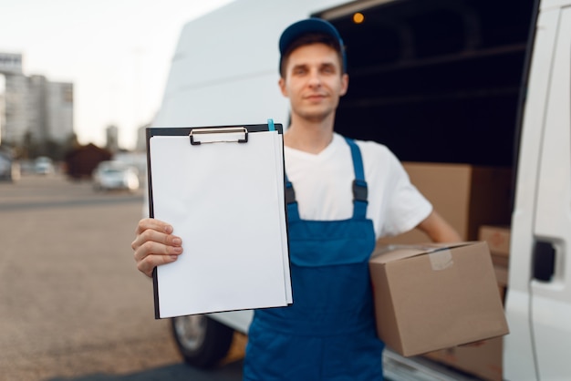 Bezorger in uniform met pakket en notitieblok, kartonnen dozen in de auto, bezorgservice.