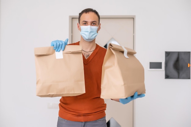 Bezorger met beschermend masker en handschoenen met doos, tas met boodschappen voor een gebouw.