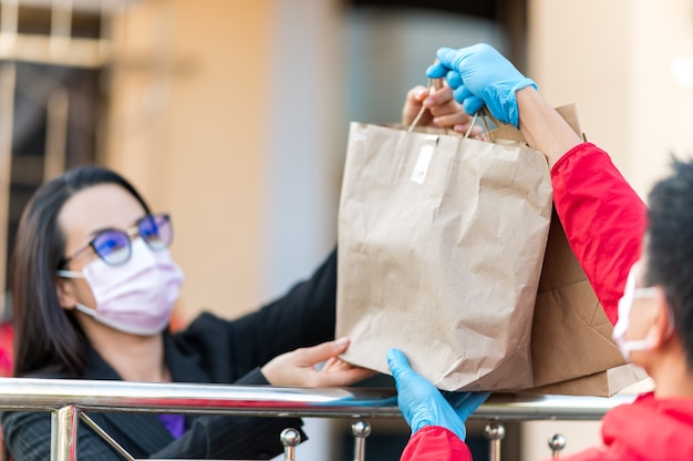 Bezorger met blauwe handschoenen bezorgt een doos aan een jonge klant bij de voordeur.