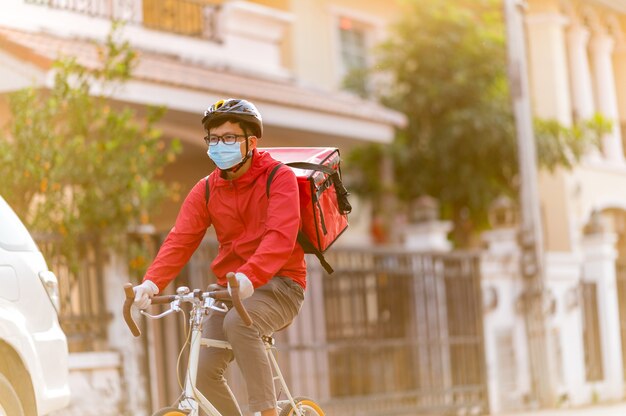 Bezorger met gezichtsbeschermend masker om coronavirus te vermijden rood uniform Fietsen om producten bij klanten thuis te bezorgen.