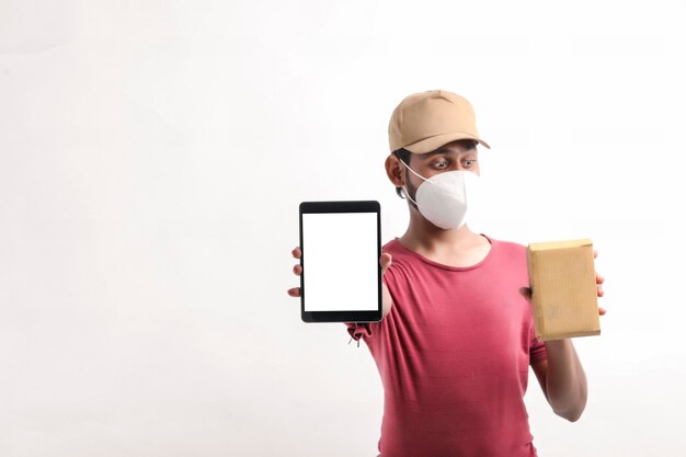 Bezorger met medisch masker en smartphone-scherm met doos in handen. Levering aan huis. Online Technologie bestellen.