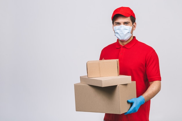 Bezorger werknemer in rode dop lege t-shirt uniforme gezichtsmasker handschoenen houden lege kartonnen doos
