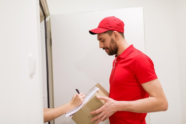 bezorging, post, mensen en verzendconcept - gelukkige man met doos en ondertekeningsformulier van de klant thuis