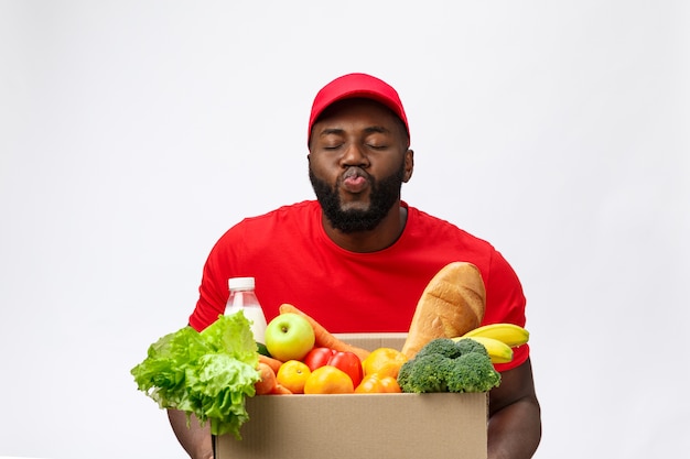 Bezorgservice - Knappe Afro-Amerikaanse bezorger die pakketdoos met boodschappen eten en drinken uit de winkel draagt.