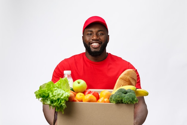 Bezorgservice - knappe afro-amerikaanse bezorger die pakketdoos met boodschappen eten en drinken uit de winkel draagt.