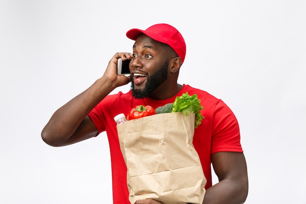 Bezorgservice - Portret van knappe Afro-Amerikaanse bezorger of koerier met boodschappenpakket en praten op mobiele telefoon om de bestelling te controleren.