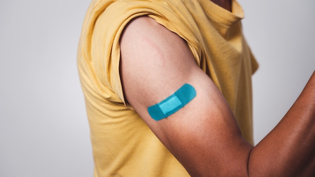 Bi-colored Asian man showing vaccinated arm with adhesive patch after getting Covid-19 vaccine injection.