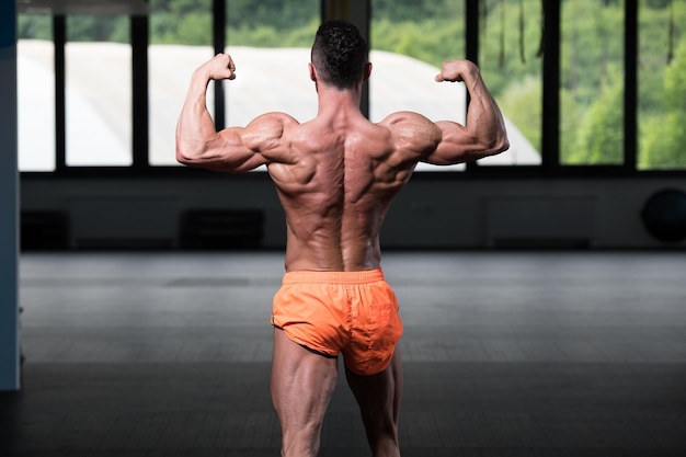 Photo biceps pose of a young man in gym