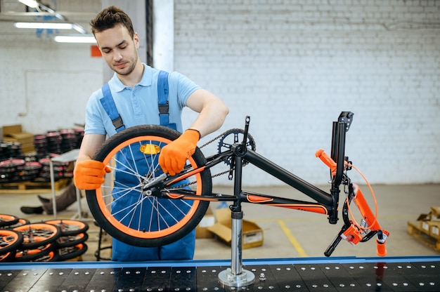 Bicycle factory, worker at assembly line, wheel installation. Male mechanic in uniform installs cycle parts in workshop