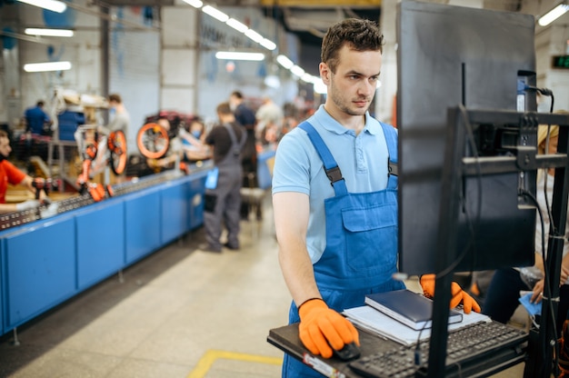 Bicycle factory, worker manages bike assembly line. Male mechanic in uniform installs cycle parts in workshop