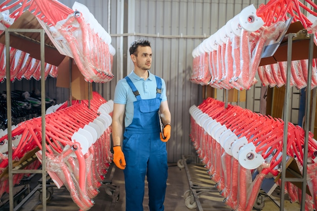 Bicycle factory, worker at the row of pink bike frames. Male mechanic in uniform installs cycle parts, assembly line in workshop