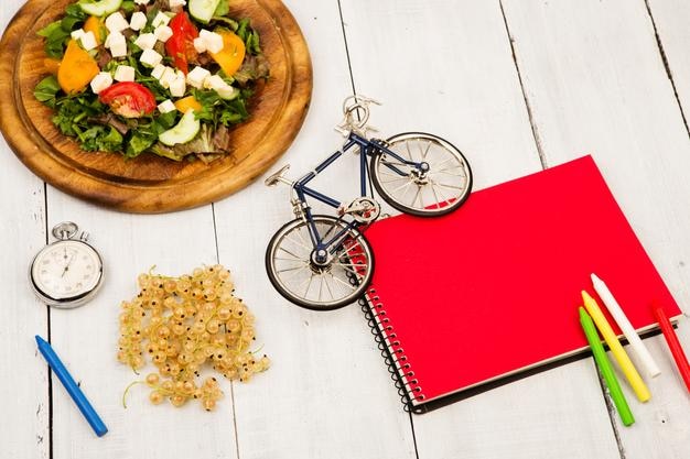흰색 나무 테이블에 신선한 야채 빨간 메모장 스톱워치와 건포도의 자전거 모델 샐러드