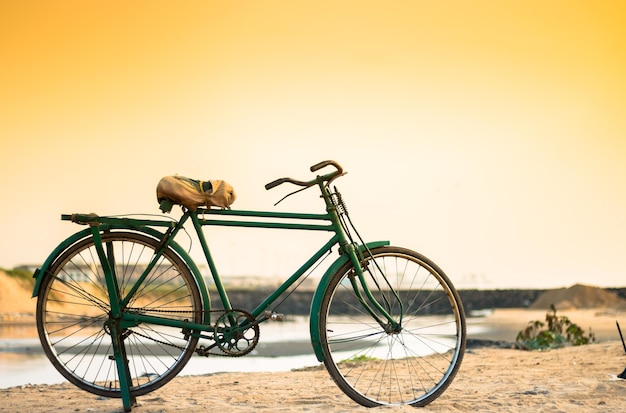 Bicycle parked by stream against clear sky during sunset