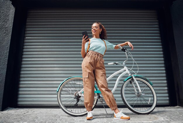 Bicycle phone and black woman in city street or urban road outdoors Bike travel and happy female from South Africa on 5g mobile tech internet browsing or social media web or online surfing