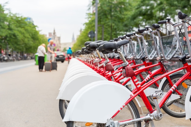 Bicycle rental, europe, bike rent parking. urban eco transport, human powered vehicle, row of red cycles, nobody