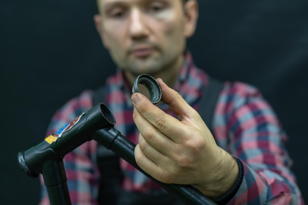 Bicycle repair The bike mechanic changes the cups and bearings in the headset of the frame Bicycle parts in the workshop on a black background The face of a young guy with a tool in his hands