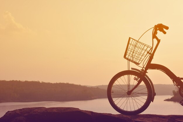 Foto bicicletta sulla roccia vicino al fiume contro un cielo limpido durante il tramonto