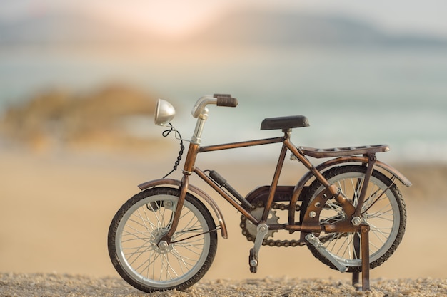 Giocattolo del trasporto di biciclette sulla spiaggia del mare della sabbia nel cielo di tramonto di sera