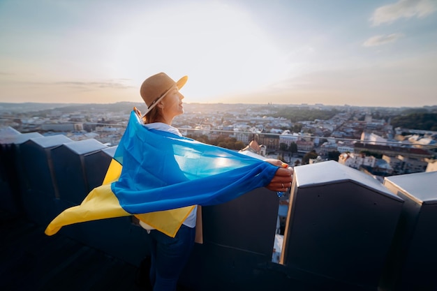 Bid voor UkrainexAA-vrouw staat met de nationale Oekraïense vlag en zwaait ermee biddend voor vrede bij zonsondergang in LvivxAA symbool van de onafhankelijkheid en kracht van het Oekraïense volk