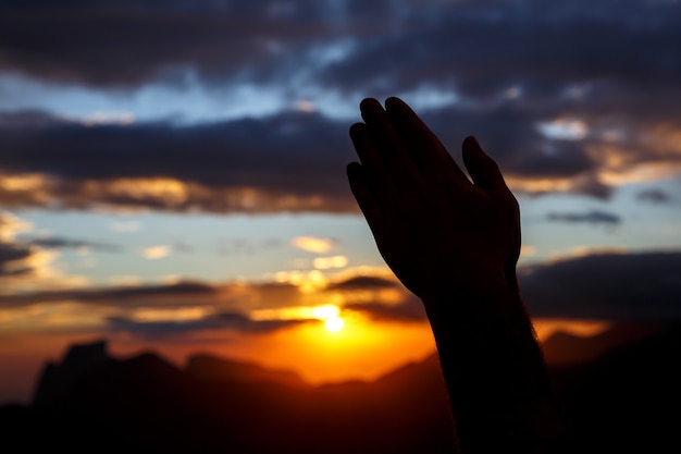 Biddende handen op zonsondergangachtergrond. Zwart silhouet