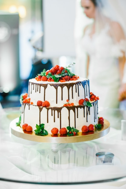 Bide staat achter heerlijke bruidstaart versierd met rode bessen en donkere chocolade