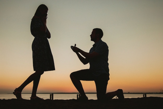 Bied je hand en hart aan op het strand tegen de achtergrond van een prachtige zonsondergang, verloving Een man geeft een ring en vraagt een meisje om te trouwen, ze is gelukkig