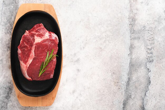 Biefstuk Vers rauw rundvlees rib eye steak met vork rozemarijn zout en peper op een grillpan op grijze stenen achtergrond Bovenaanzicht Mockup voor ontwerpidee