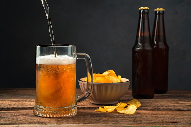 Bier gieten in een glas tegen de achtergrond van chips en bierflesjes