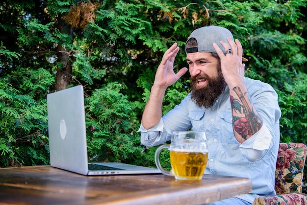 Bier helpt hem te ontspannen na een zware dag Brute man vrije tijd met bier en laptop Eindelijk vrijdag Hipster ontspannen zitterras met bier Bebaarde hipster freelancer geniet van het einde van de werkdag met een bierpul