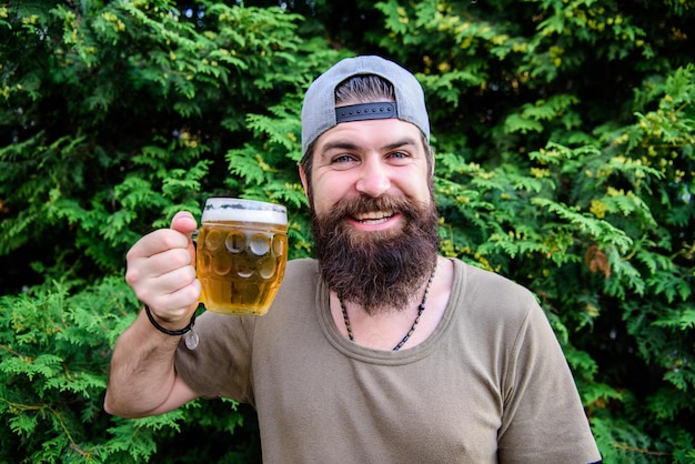 Foto bier is een geweldig zomerdrankje bebaarde man met biermok in de zomer natuur brutale hipster verfrissend bier drinken op zomerdag gelukkig drinker genieten van zomertijd