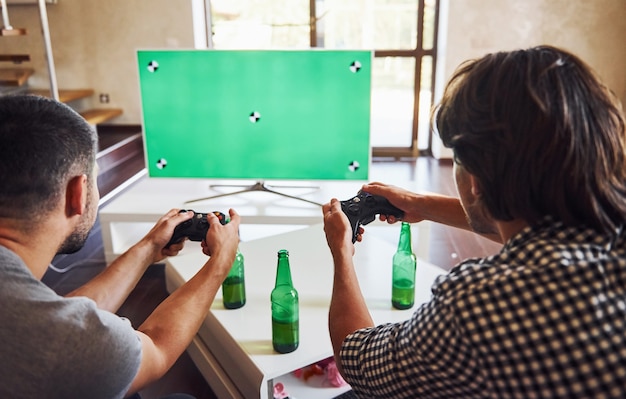 Bier op tafel. Groep vrienden hebben plezier met het spelen van consolegames binnenshuis in de woonkamer.