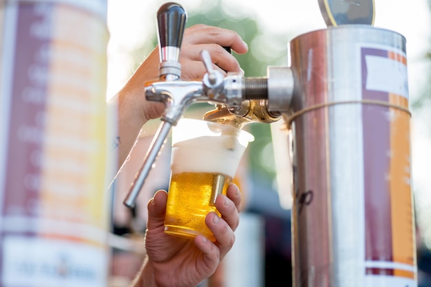 Bier wordt uit een kraan in een glas gegoten De barman giet bier in een plastic glas