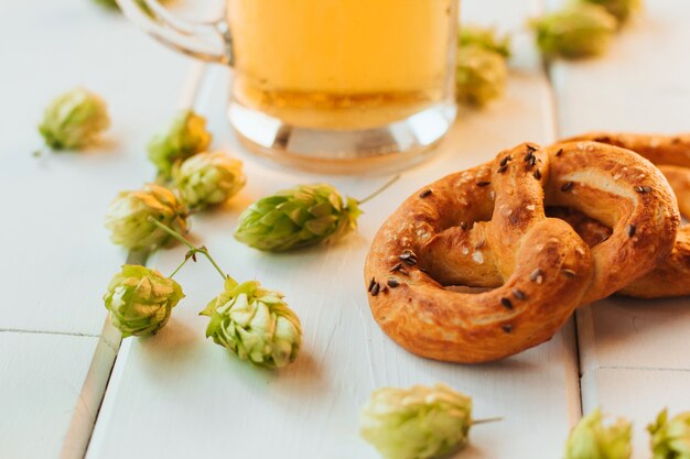 Bierpul, hopbellen en pretzels op een witte houten tafel.