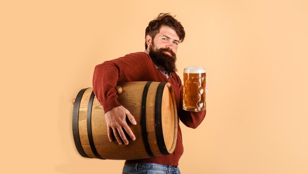 Biertijd aantrekkelijke bebaarde mannelijke brouwer met mok bier en houten vat biervakantiedrankjes