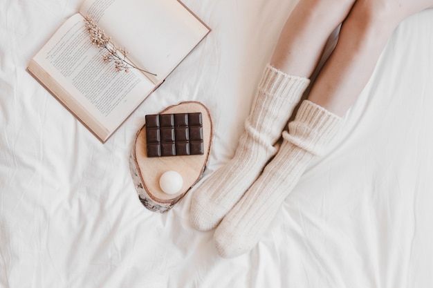 Foto bies de benen in de buurt van chocolade en boek op bed