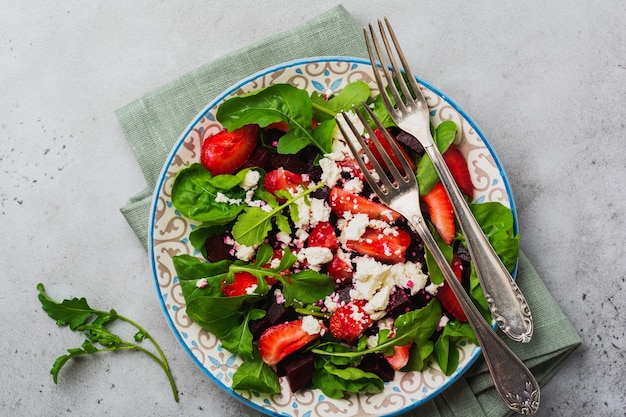 Bieten, aardbeien, fetakaas en rucola salade in keramische plaat op oude betonnen tafel achtergrond.