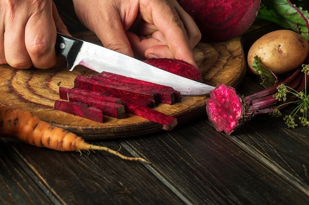 Bieten of rode biet snijden door de handen van een chef-kok op een snijplank voor het koken van dieetvoeding in de keuken