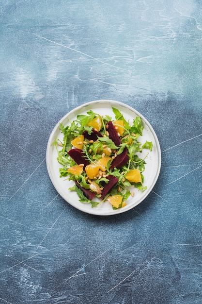 Bieten, sinaasappel, pijnboompitten, olijfolie, fetakaas en rucola salade in keramische plaat op oude betonnen tafel