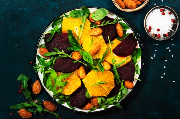 Bietensalade met oranje rucola en amandelen op blauwe tafelachtergrond Veganistisch gezond voedsel Kopieer ruimte