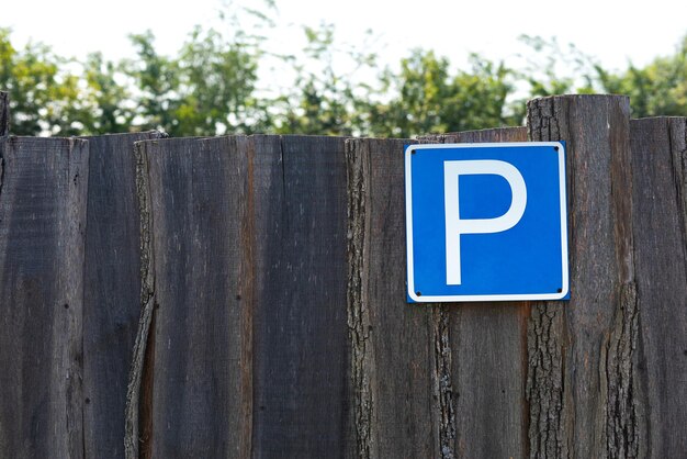 Photo big blue parking sign, leaning against old wooden white cattle fence, a farm house.