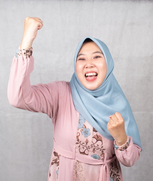 Foto grande bonus. donna asiatica allegra in hijab che celebra il successo, alzando le mani e stringendo i pugni