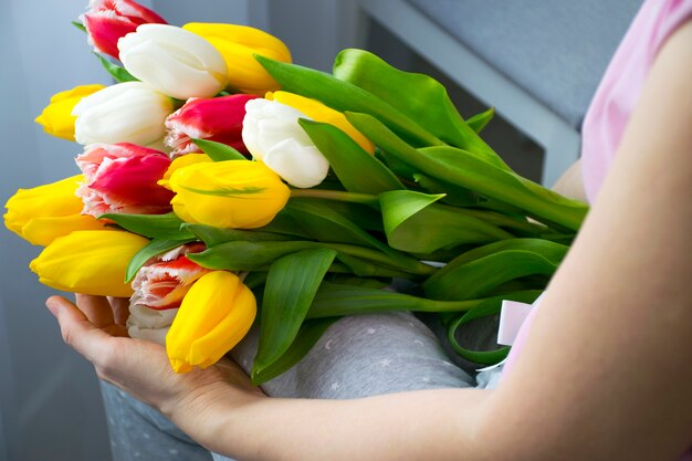 Большой букет красивых цветов разноцветных тюльпанов на коленях женщины в домашней одежде
