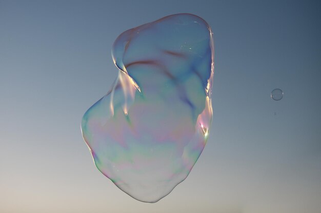 青い空の上を飛んでいる大きな泡巨大なカラフルなシャボン玉が曇り空の背景の上を飛んでいます