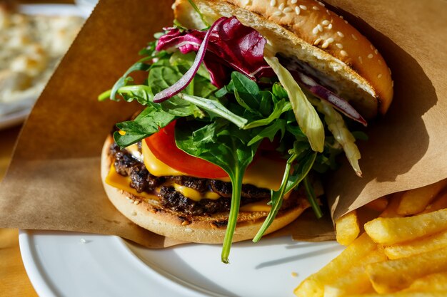 Big burger with beef cutlet and salad in a paper envelope.