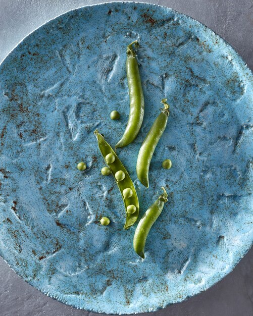 Foto un grande piatto di ceramica con cibo vegetariano biologico crudo - baccelli verdi con piselli e piccoli fagioli di piselli. concetto di cibo disintossicante pulito. vista dall'alto.