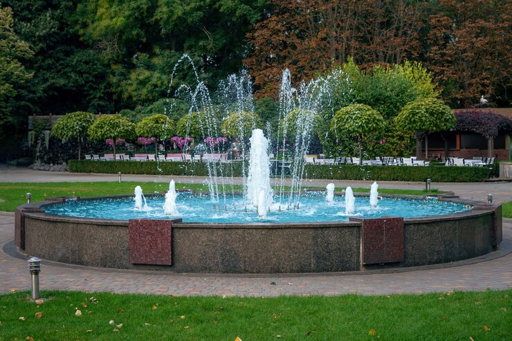 Photo big city beautiful working fountain in a public place in the bright autumn sun. trees and bushes in the parking.
