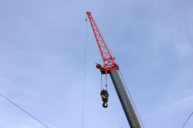 Big construction arm crane with heavy hook on metal cable in clear blue sky