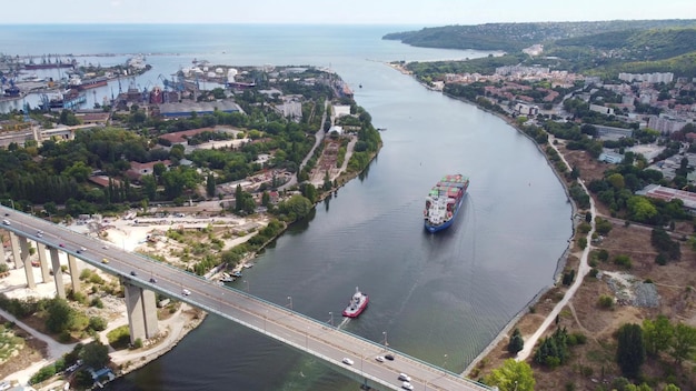 La grande nave portacontainer si muove attraverso la baia sotto un ponte autostradale con traffico intenso vista aerea