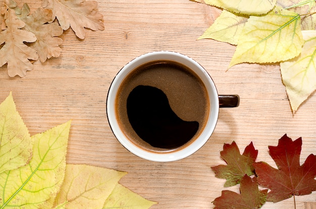 A big cup of coffee surrounded by autumn leaves. 